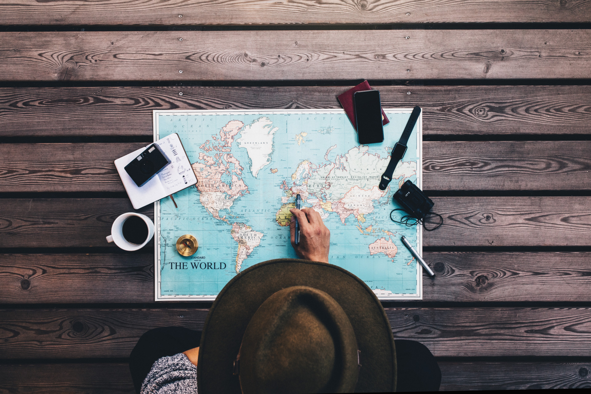 Persona con il cappello da viaggiatore che sta guardando una mappa del mondo e sta bevendo un caffè