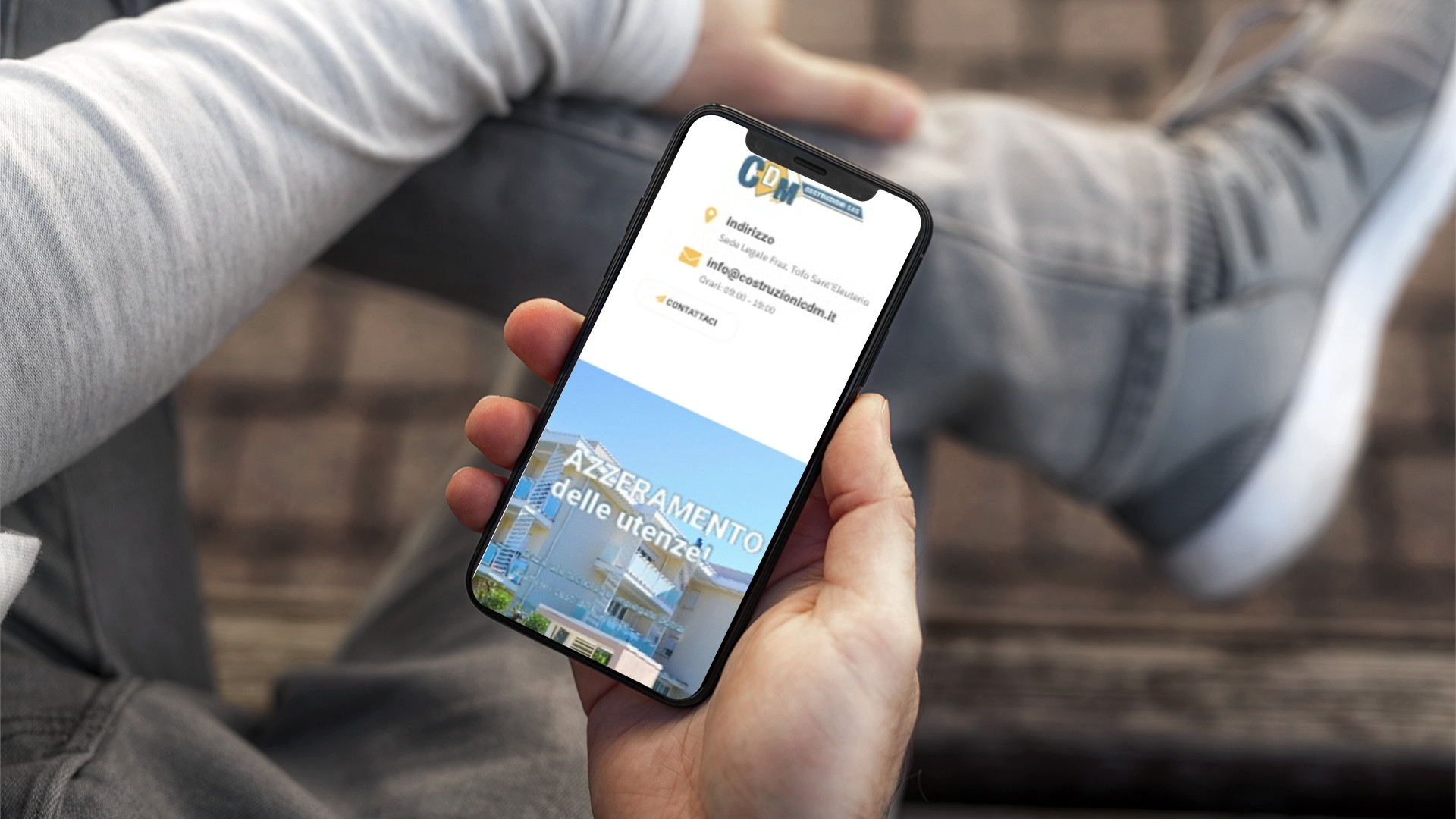 Mano con iPhone che mostra il sito web in modalità mobile responsive di Costruzioni CDM di Teramo
