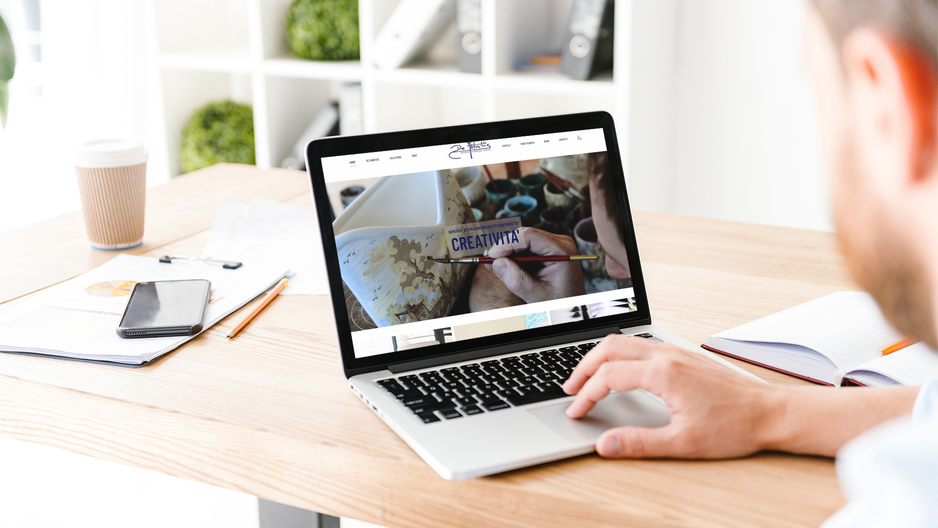 Mockup ragazzo mentre guarda sul MacBook sulla scrivania con Home Page del Sito dell'azienda De Fabritiis di Castelli Teramo