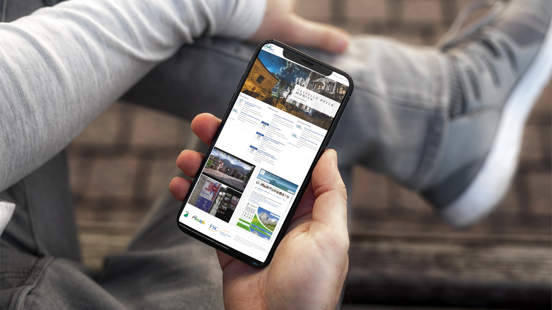 Mano con iPhone che mostra il sito web in modalità mobile responsive della DMC Gran Sasso Laga di Teramo