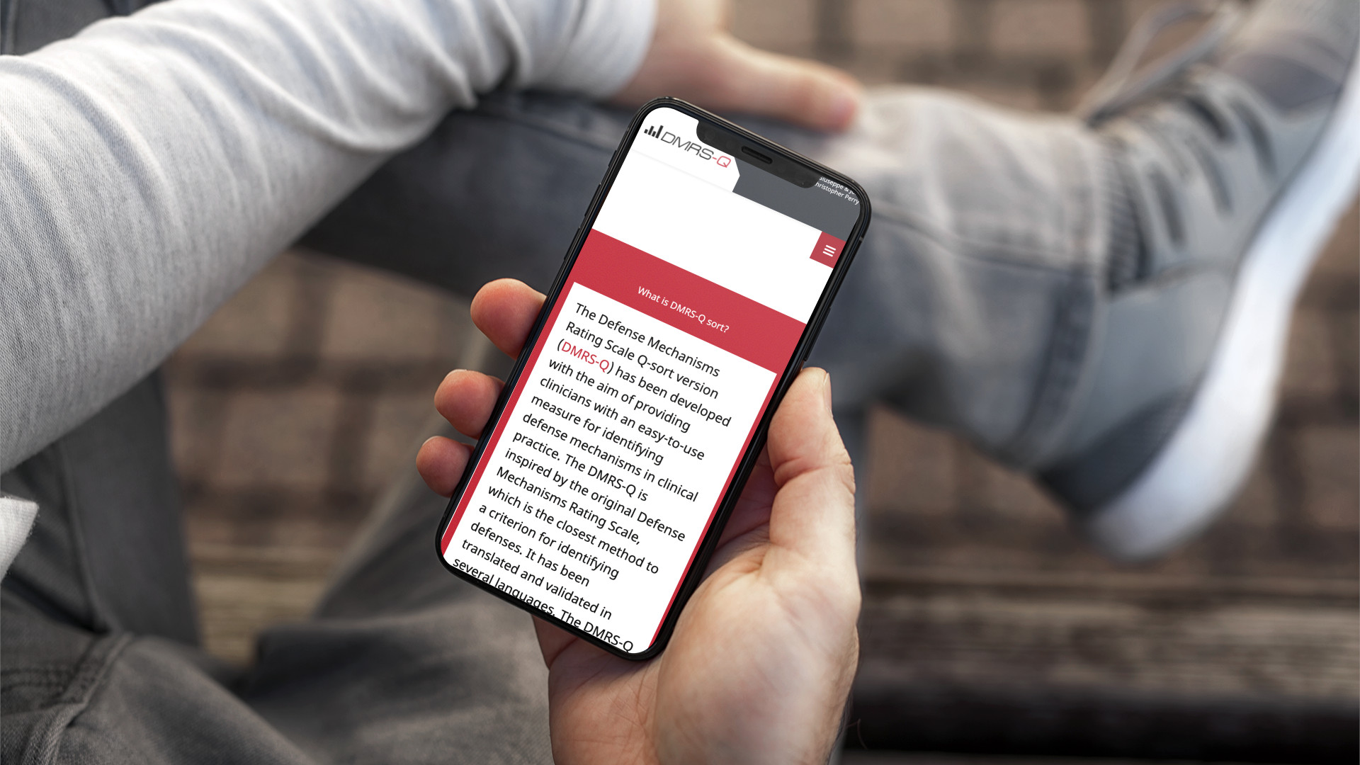 Mano con iPhone che mostra il sito web in modalità mobile responsive di DMRS-Q Sort