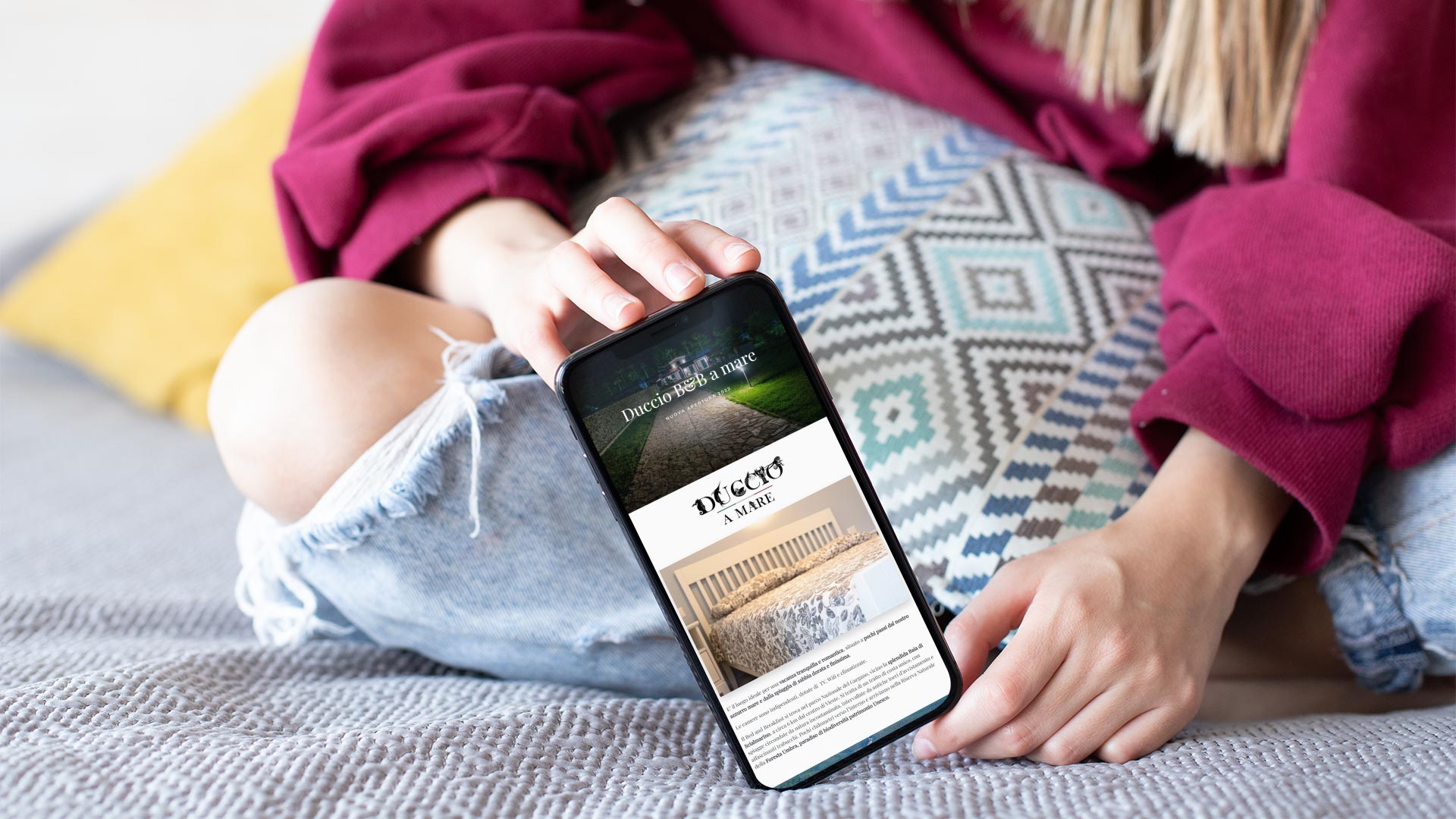 Ragazza seduta sul letto mostra su smartphone la home page del Sito Web Duccio a Mare B&B Vieste