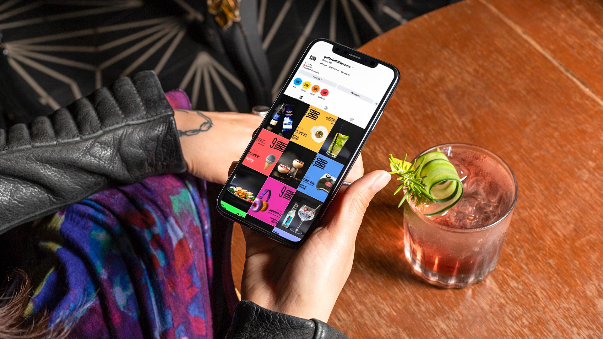 Donna con cocktail mentre guarda la pagina Instagram Galleria 900 Teramo su iPhone XS