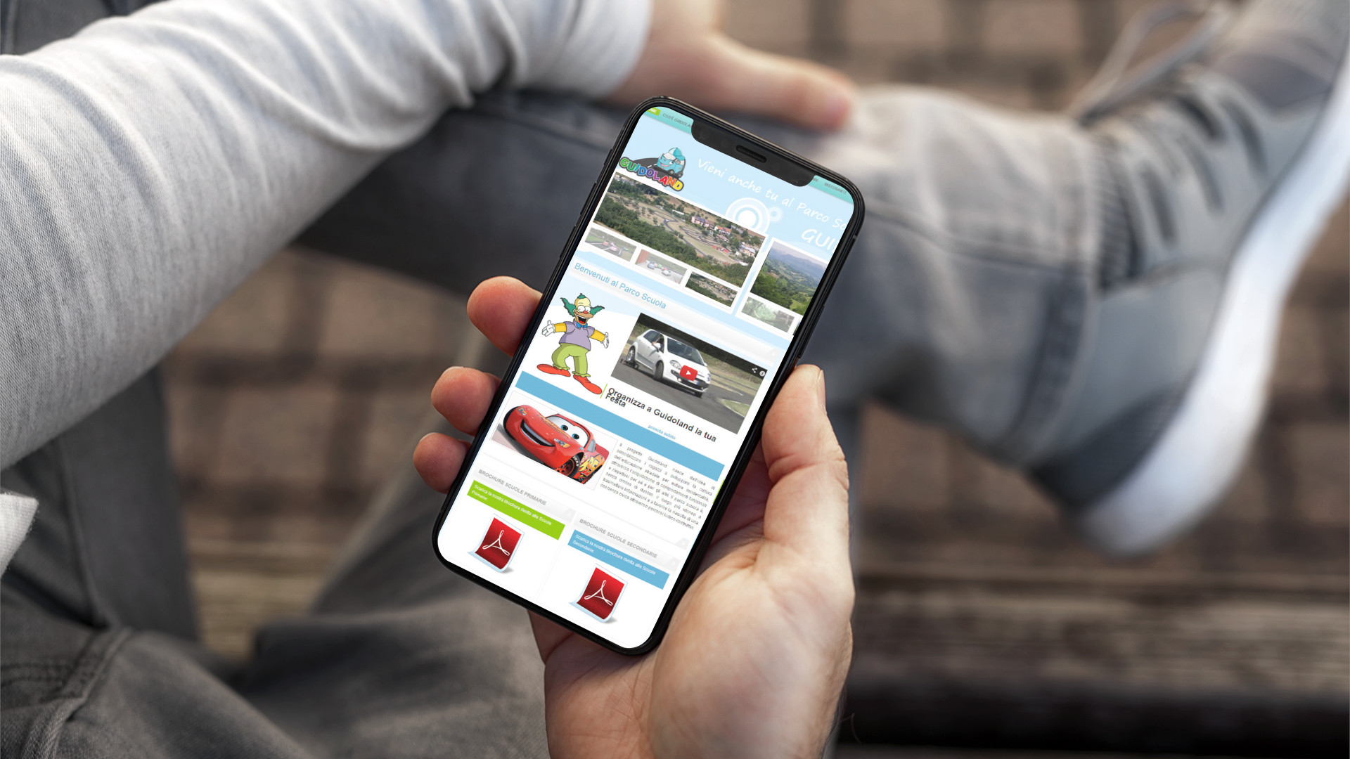 Mano con iPhone che mostra il sito web in modalità mobile responsive di Guidoland di Ascoli Piceno