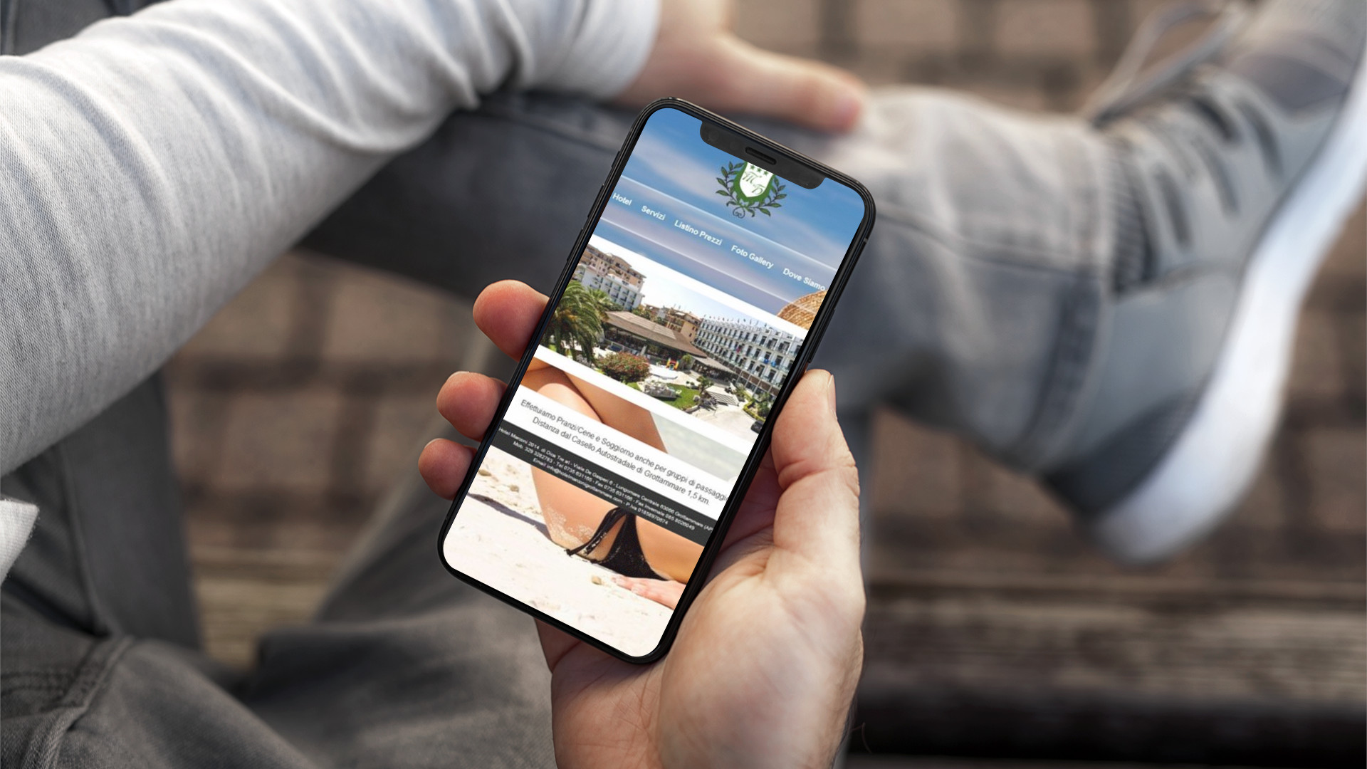 Mano con iPhone che mostra il sito web in modalità mobile responsive dell'Hotel Marconi di Grottammare