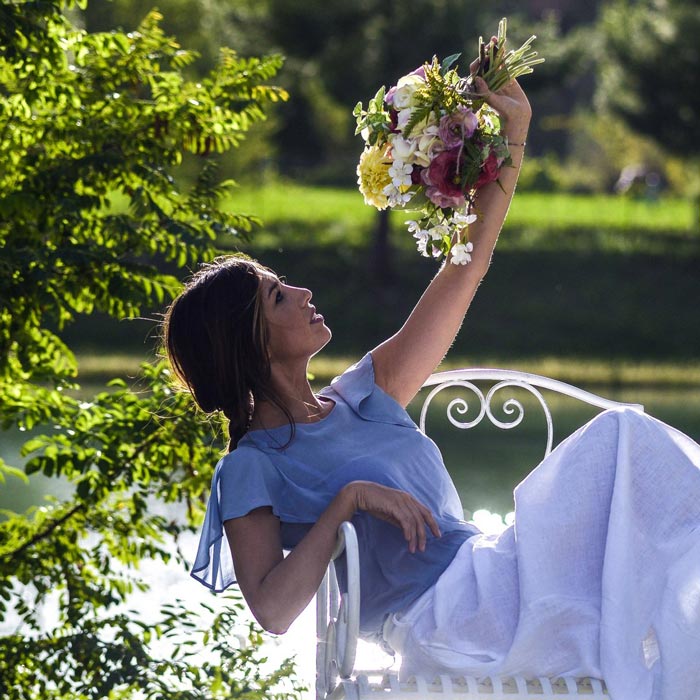 Modella seduta in giardino mentre solleva un mazzo di fiori