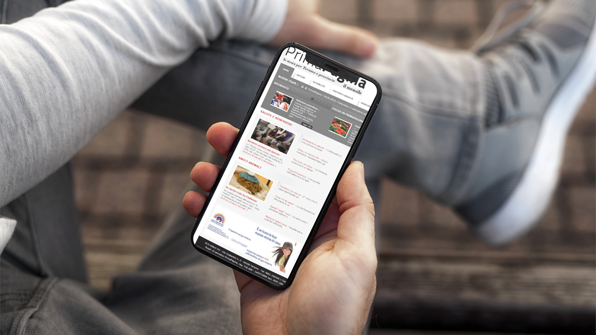 Mano con iPhone che mostra il sito web in modalità mobile responsive di Prima Pagina