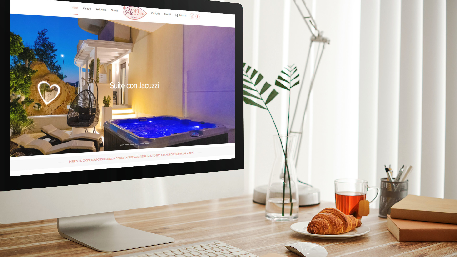 Mockup iMac sulla scrivania durante la colazione con home page del sito web Residence AleDen Vieste