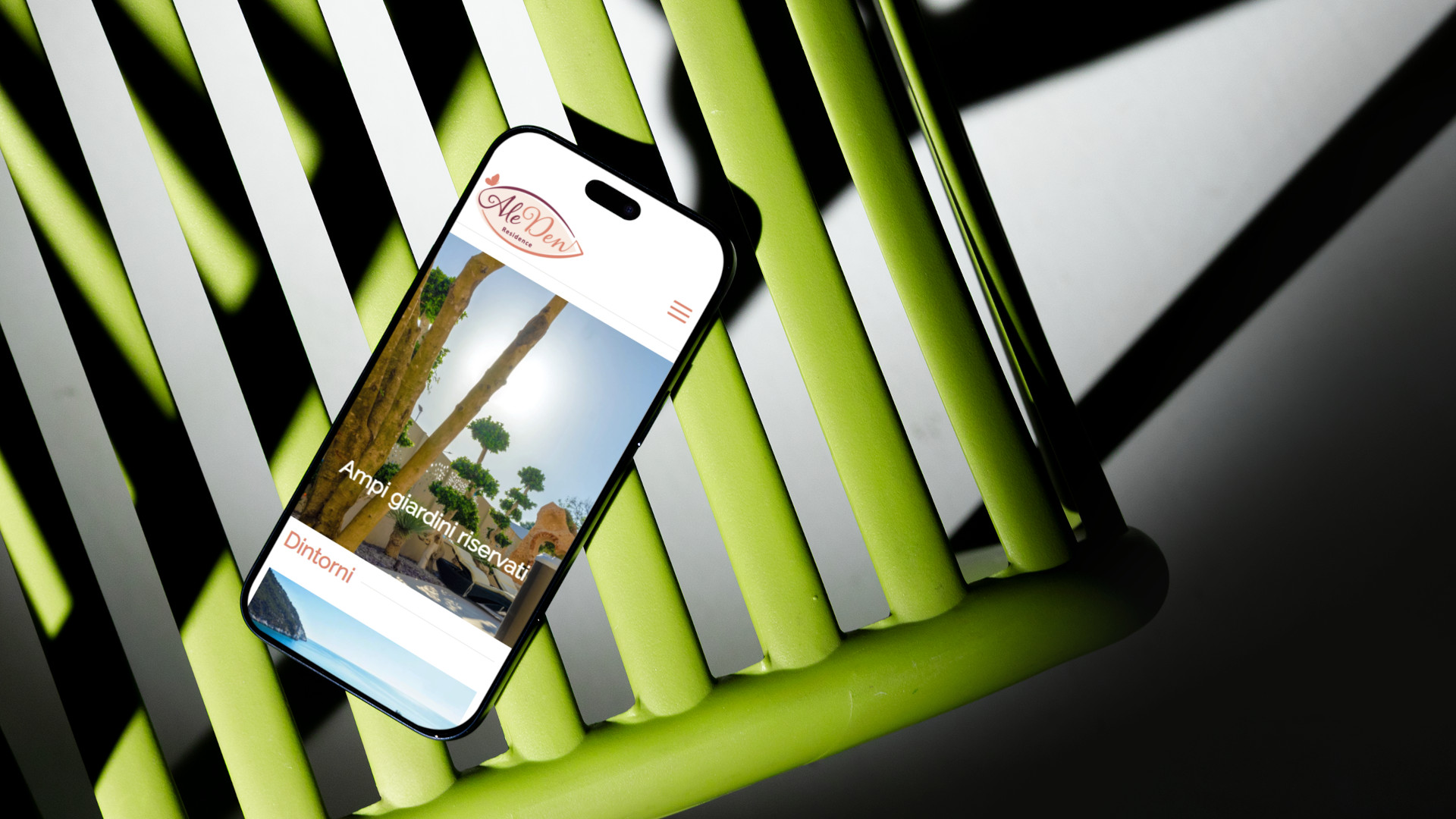 Mockup smartphone poggiato sulla sedia verde con sito web responsive Residence AleDen Vieste