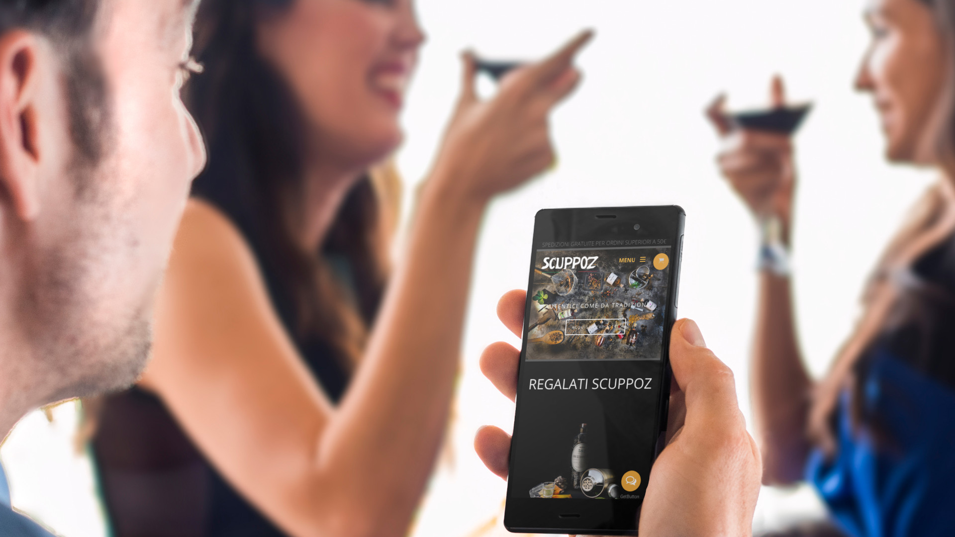 Ragazzo con due ragazze a cena che visualizza il sito web responsive di Scuppoz Liquori in versione mobile