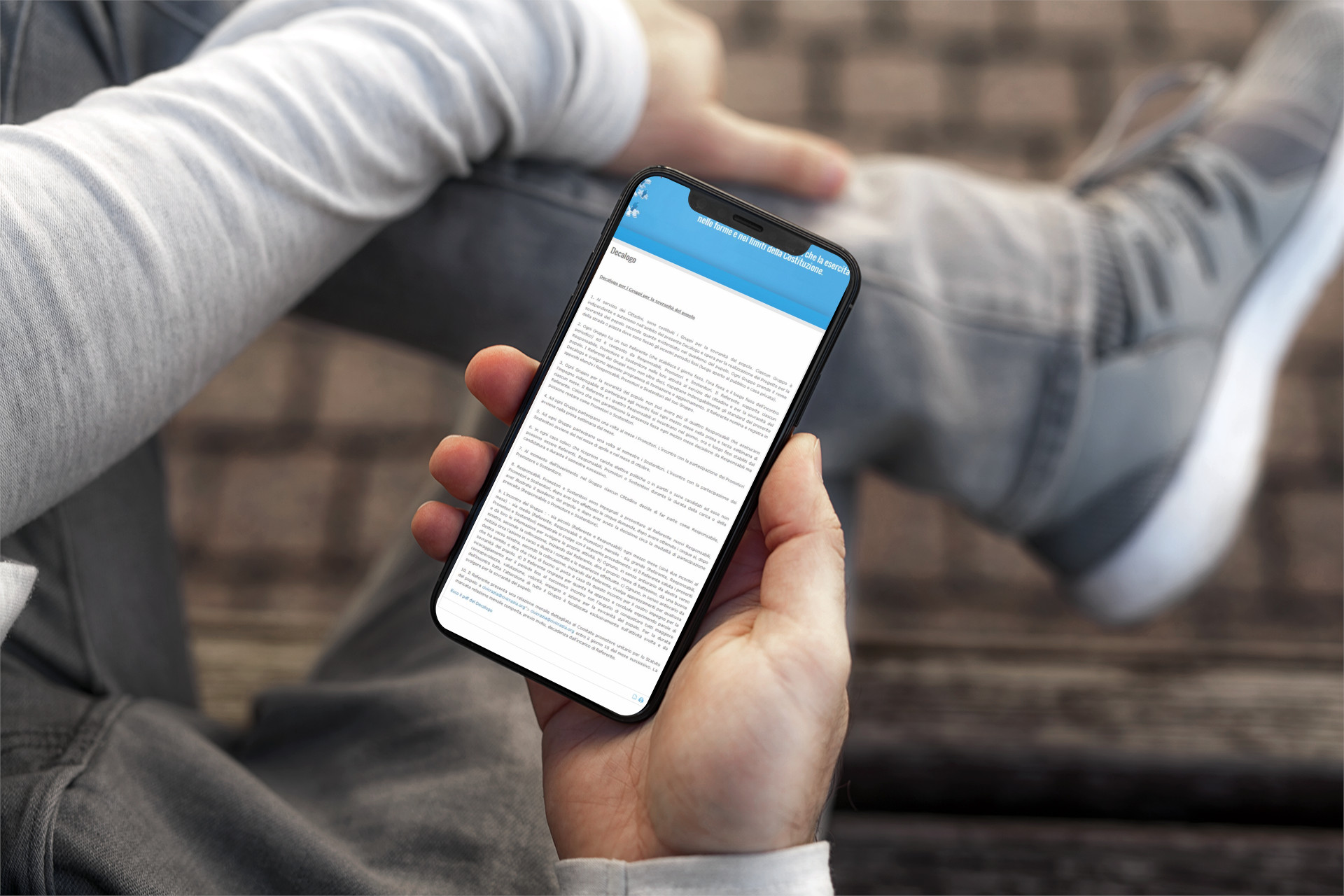 Mano con iPhone che mostra il sito web in modalità mobile responsive della Sovranità Del Popolo
