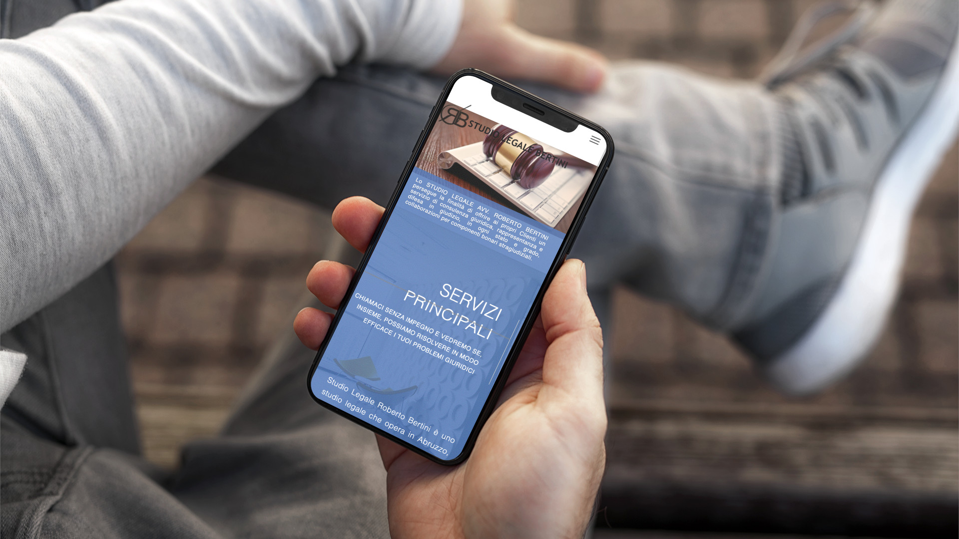 Mano con iPhone che mostra il sito web in modalità mobile responsive dello Studio Legale Bertini di Teramo