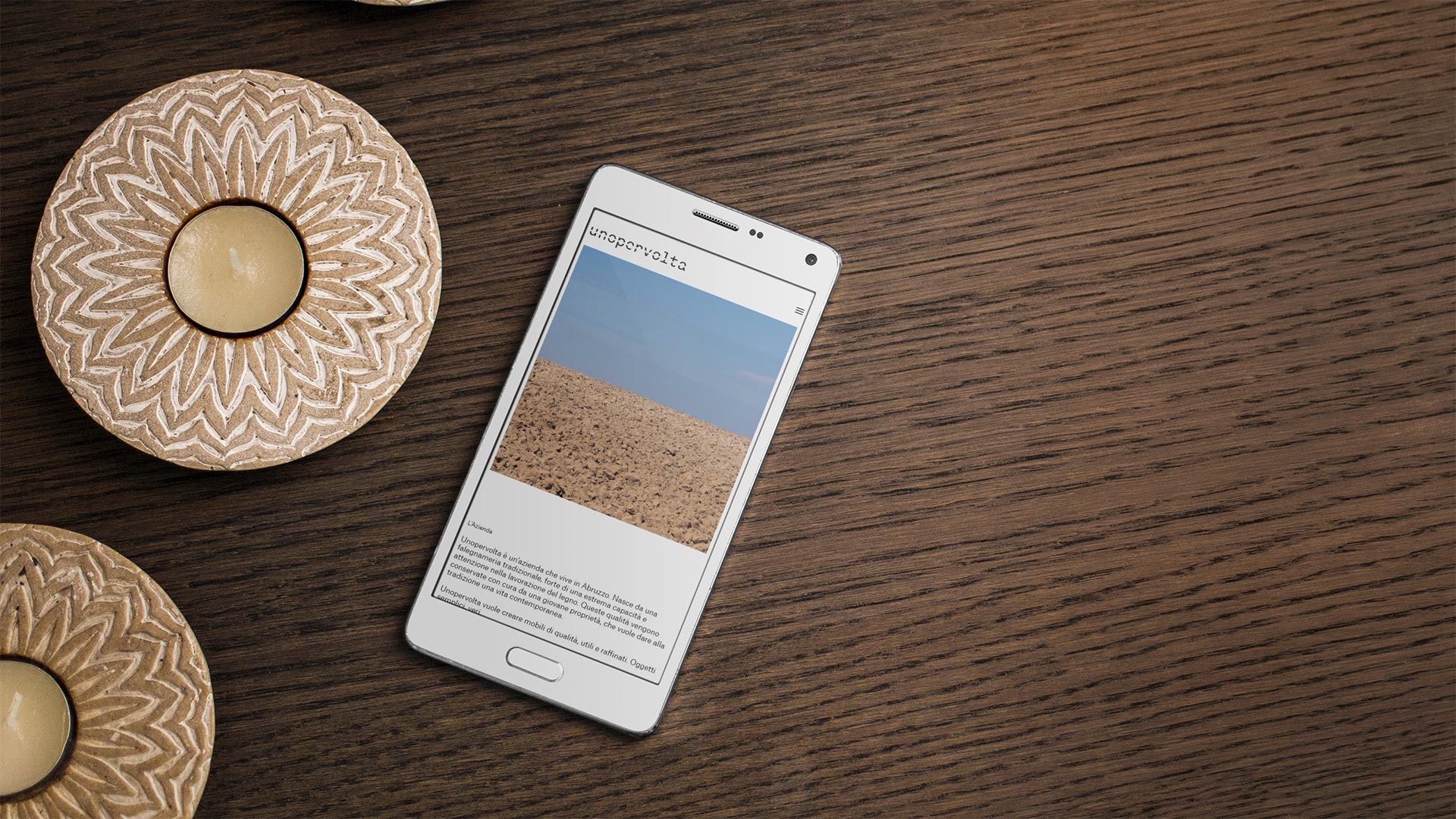 Smartphone Android su tavolo in legno con candele mostra il Sito Web unopervolta.it