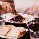 Donna taglia carne alla griglia servita con pane e vino rosso