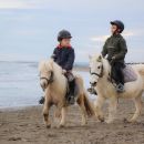 Due bambini montano pony bianchi durante una passeggiata sulla spiaggia