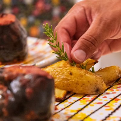Mano che completa un piatto di carne con patate e rosmarino