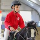 Bambina con felpa rossa in sella a un pony durante una gara indoor