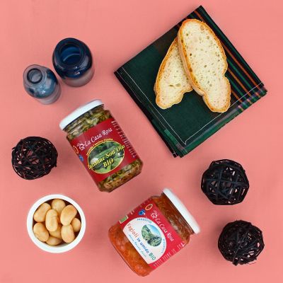 Conserve di verdure sottolio con pane in una composizione food su sfondo rosa