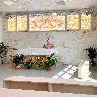 Sala del commiato con composizioni floreali, panche e vetrata colorata