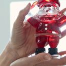 Mano che regge una statuina di Babbo Natale in vetro rosso