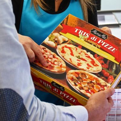 Cliente mostra una confezione di pizza davanti ai banchi dei surgelati