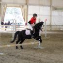 Bambina su un pony nero mentre supera un ostacolo nel campo coperto