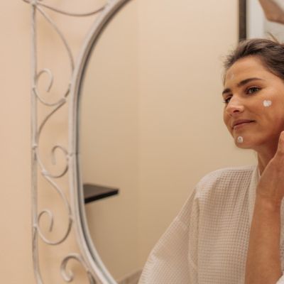 Donna davanti allo specchio mentre applica una crema sul viso
