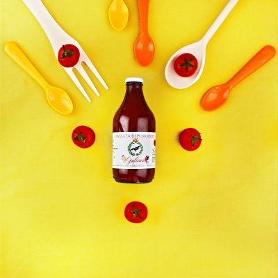 Bottiglia di passata di pomodoro abruzzese con pomodori e posate su sfondo giallo