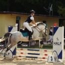 Amazzone con cavallo grigio mentre supera un ostacolo bianco