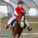 Bambina in divisa rossa su un cavallo baio nel campo coperto