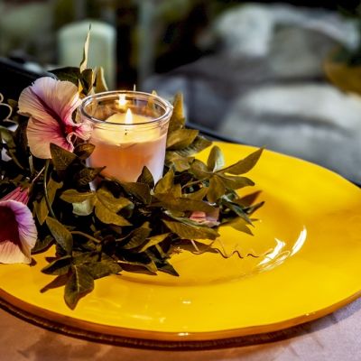 Piatto rotondo in vetro giallo con candela e composizione floreale