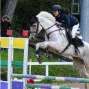 Amazzone con cavallo grigio mentre supera un ostacolo colorato