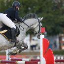 Amazzone con cavallo grigio durante il salto di un ostacolo rosso