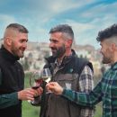 Tre ragazzi proprietari Tenuta Trium con calici vino sfondo paese di Notaresco Teramo Abruzzo