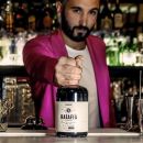 Ragazzo dietro bancone bar che mostra bottiglia ratafià Scuppoz su Instagram a Teramo in Abruzzo