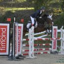 Amazzone con cavallo baio mentre supera un ostacolo rosso e bianco