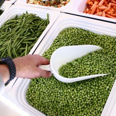 Piselli surgelati sfusi raccolti con una paletta dal banco freezer