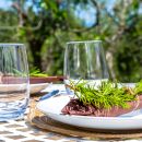Tavola apparecchiata all'aperto con calici e rametti aromatici