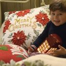 Bambino sorridente con un cuscino ricamato Merry Christmas