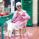 Donna con abito rosa e occhiali da sole seduta in un allestimento colorato