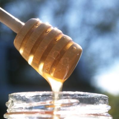 Miele che cola da un apposito cucchiaio dentro un vasetto