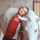 Bambino disteso sul dorso di un cavallo bianco durante un'attività assistita